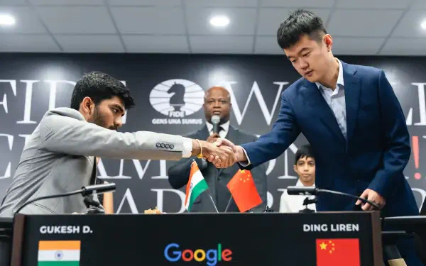 Gukesh Dommaraju and Ding Liren shake hands before their match at the World Chess Championship, with a backdrop featuring national flags and a Google logo.