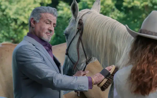 Sylvester Stallone in a scene from the TV show Tulsa King, tenderly brushing a white horse, set against a lush, green background. A striking 4K Ultra HD image.