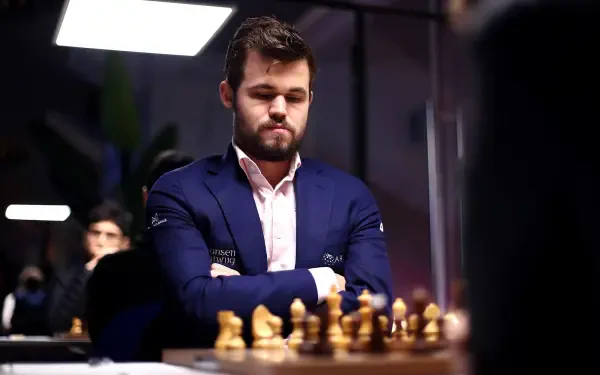 Magnus Carlsen, the renowned chess player, is deep in thought during a match, with chess pieces in front of him. This HD wallpaper captures the intensity of competitive chess.