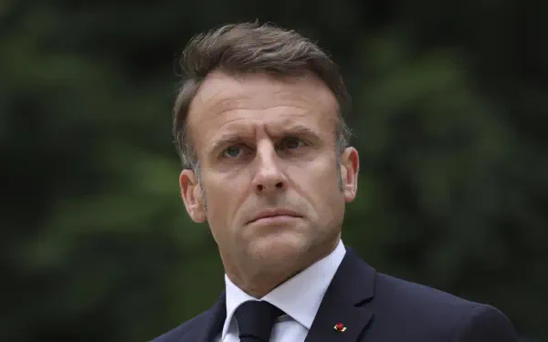 A high-definition desktop wallpaper of Emmanuel Macron, featuring him with a serious expression against a blurred natural background.