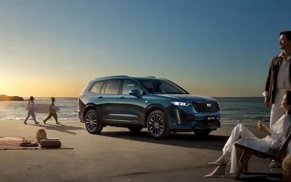 A sleek Cadillac XT6 SUV is parked on a beach at sunset, showcasing its modern design against a serene coastal backdrop, making a striking 4K Ultra HD wallpaper.