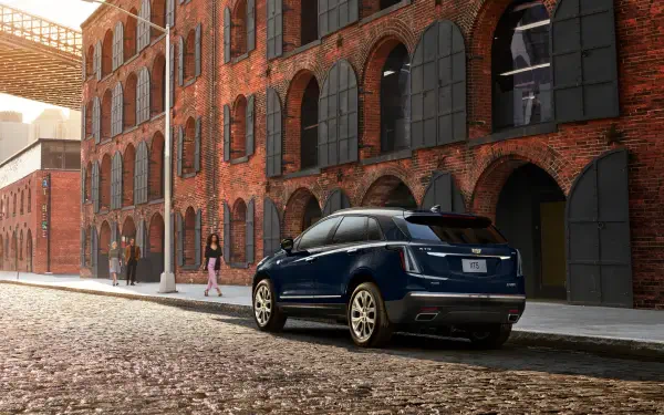 A sleek Cadillac XT5 parked on a cobblestone street in front of historic red-brick buildings, showcasing modern elegance against a classic backdrop. Ideal for an HD PC wallpaper.