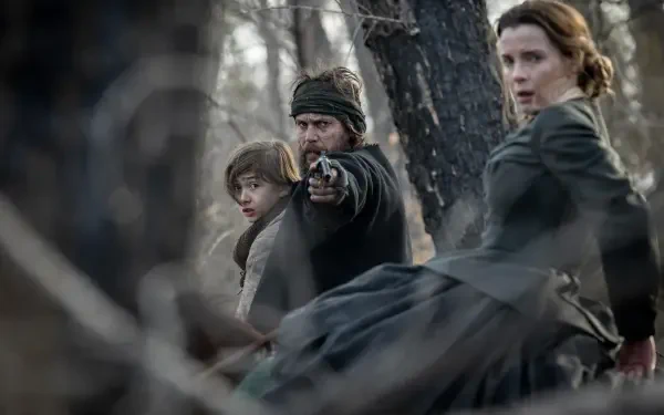 Three characters from the TV show American Primeval are captured in this HD desktop wallpaper, set against a wooded backdrop, conveying tension and drama.