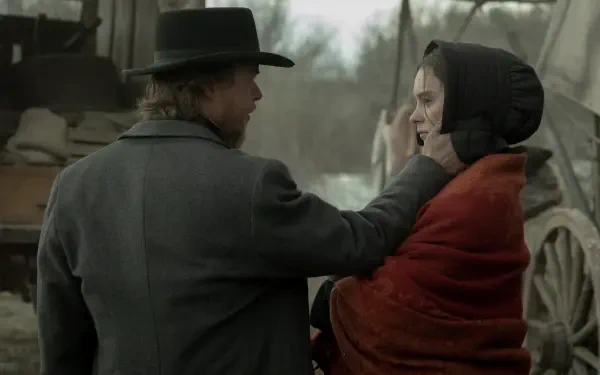 A dramatic moment from the TV show American Primeval, featuring a man in a hat and a woman wrapped in a red blanket, set against a rustic background. HD desktop wallpaper.