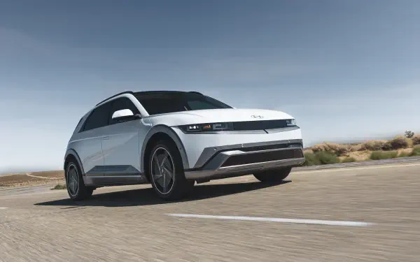 A sleek Hyundai IONIQ 5 drives along a deserted road under a clear blue sky, showcasing its modern design. This stunning 4K Ultra HD wallpaper highlights the car's features beautifully.
