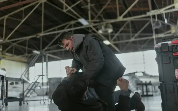 A dramatic scene from the TV show The Night Agent, featuring Gabriel Basso in an intense confrontation, set in an industrial environment. High-definition desktop wallpaper.