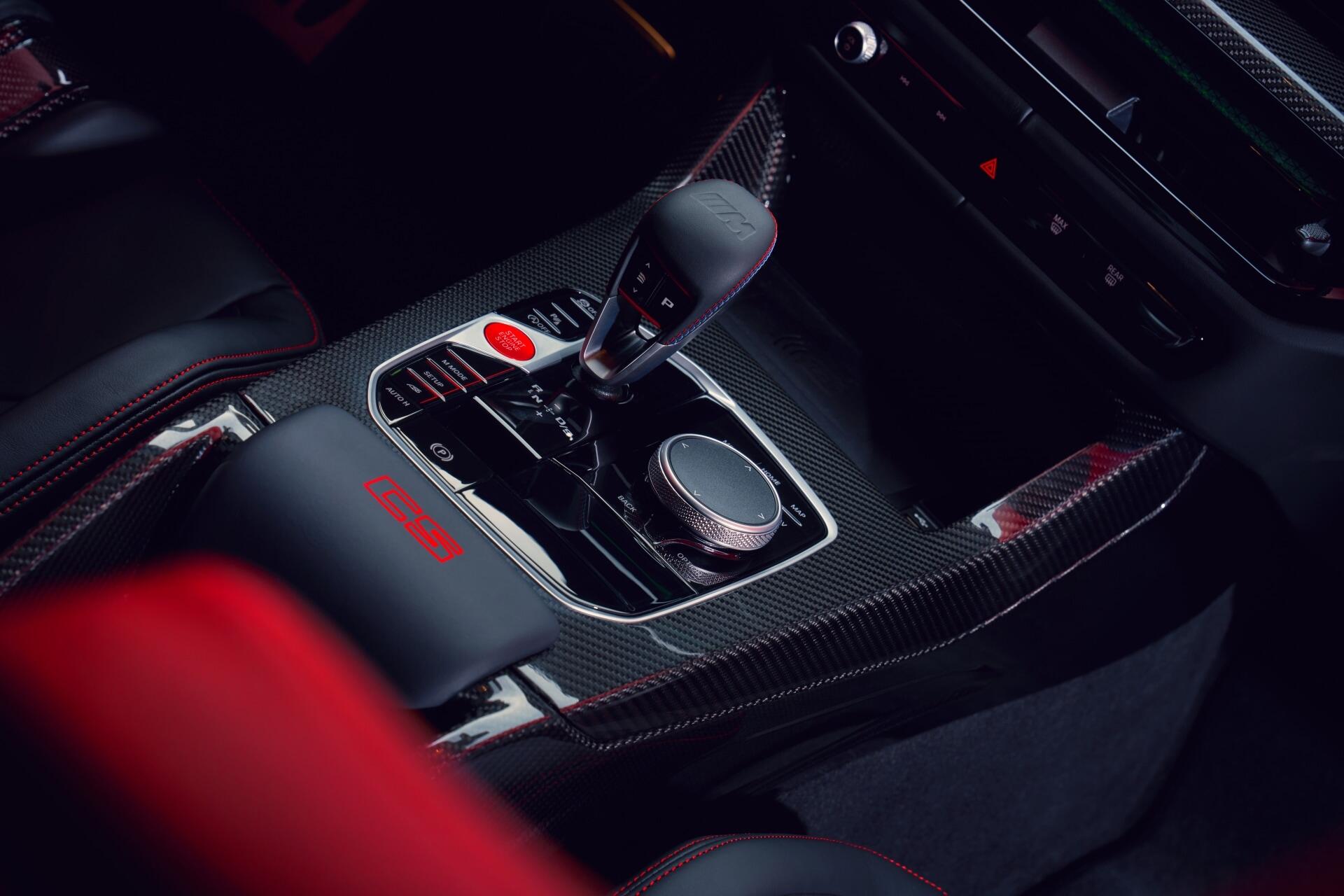 Close-up view of the interior of a BMW M3 CS Touring, featuring a sleek console with gear shift, buttons, and carbon fiber accents, designed for a high-performance driving experience.
