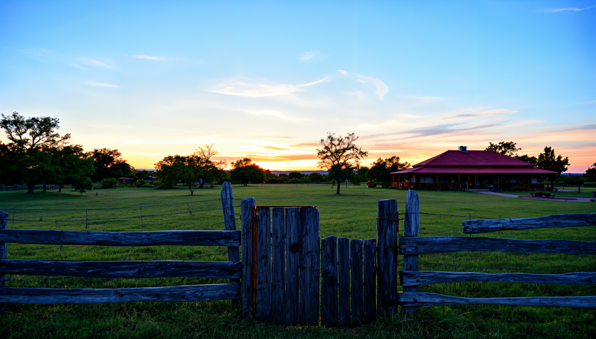 A serene ranch scene in 4K Ultra HD showcases a wooden fence gate with a lush green pasture and a charming red-roofed building against a vibrant sunset sky.