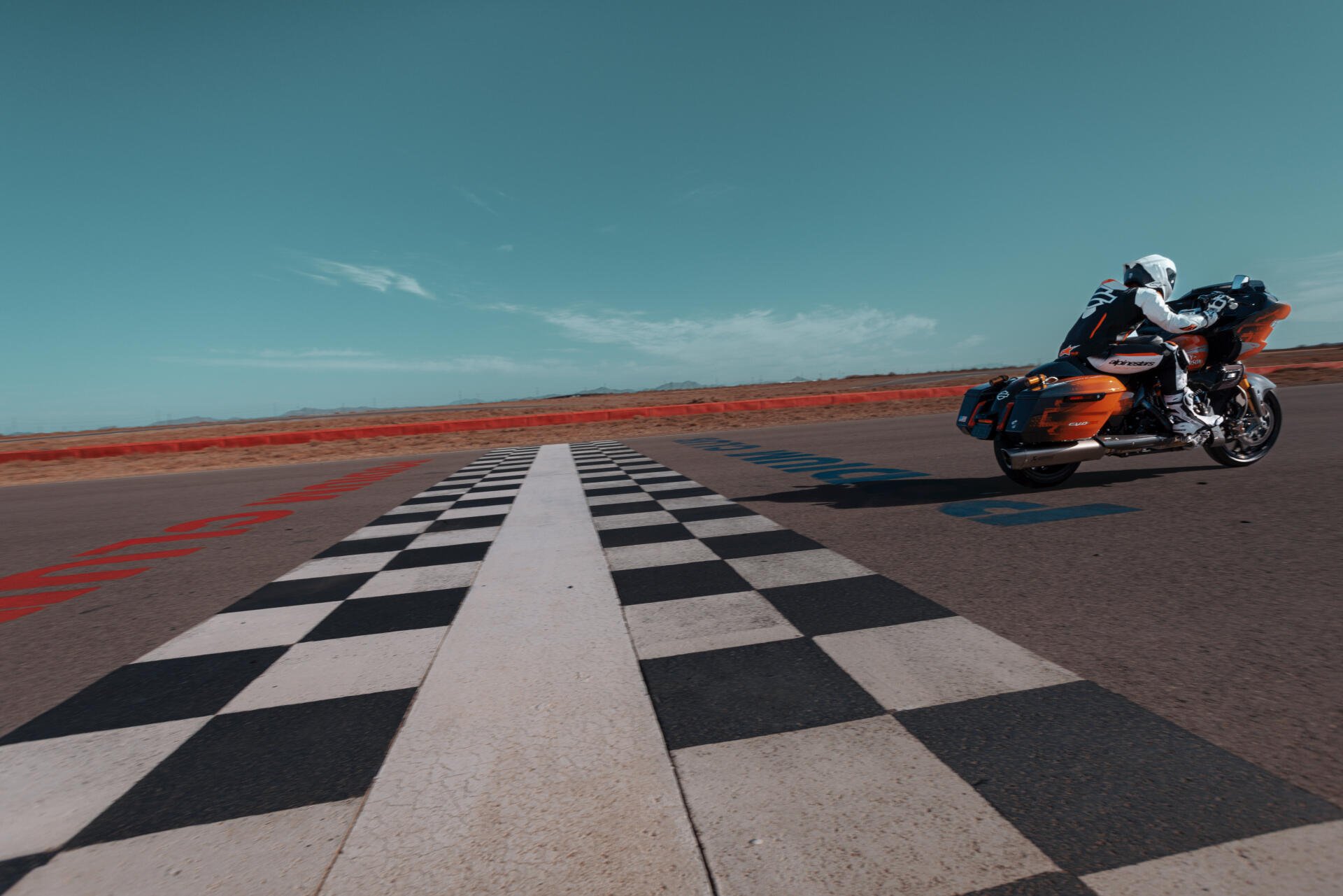 A Harley-Davidson CVO Road Glide RR takes a sharp curve on a checkered racetrack, set against a vibrant blue sky, showcasing its sleek design in this dynamic 4K Ultra HD wallpaper.