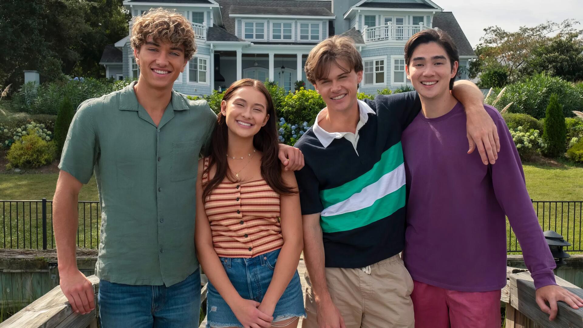 HD PC desktop wallpaper of four smiling young adults from the TV show The Summer I Turned Pretty, standing together outdoors in front of a large house.