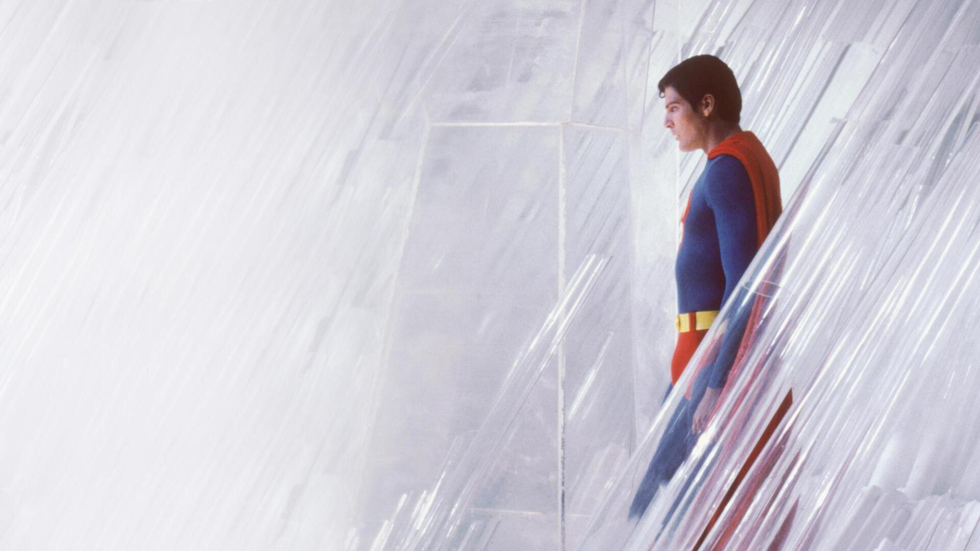 Superman (1978) in blue-and-red suit, side profile beside a crystalline wall; HD PC desktop wallpaper and background with soft light and minimalist composition.