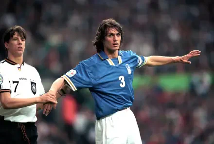 A dynamic moment featuring Paolo Maldini in the blue jersey of the Italy National Football Team, showcasing his iconic defensive skill in a match against Germany. HD desktop wallpaper.
