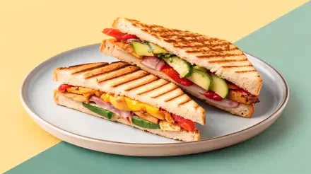 A close-up of two delicious panini sandwiches on a light blue plate, showcasing vibrant fillings of vegetables and melted cheese, set against a soft, colorful background. 