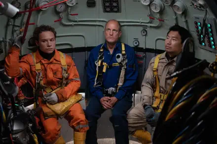 Three men in diving suits sit inside a futuristic vessel, showcasing a tense moment from the movie Last Breath (2025) featuring Finn Cole, Woody Harrelson, and Simu Liu.