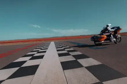 A Harley-Davidson CVO Road Glide RR takes a sharp curve on a checkered racetrack, set against a vibrant blue sky, showcasing its sleek design in this dynamic 4K Ultra HD wallpaper.
