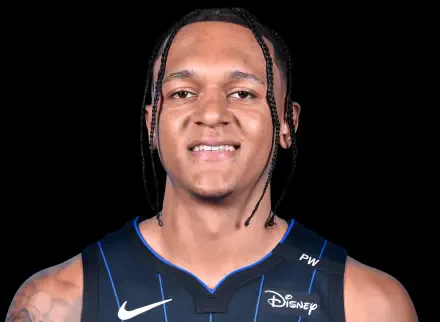 A close-up of Paolo Banchero, NBA player for the Orlando Magic, smiling confidently in his team jersey, set against a solid black background.