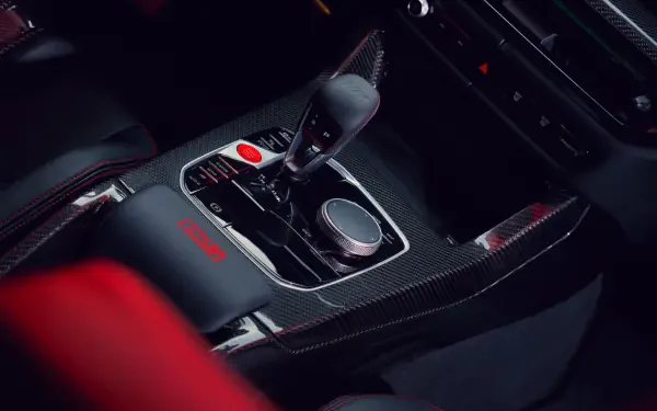 Close-up view of the interior of a BMW M3 CS Touring, featuring a sleek console with gear shift, buttons, and carbon fiber accents, designed for a high-performance driving experience.