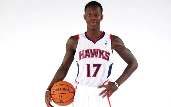 Dennis Schröder, wearing an Atlanta Hawks jersey, poses confidently with a basketball. This NBA-themed HD wallpaper captures the spirit of sports and basketball enthusiasm.