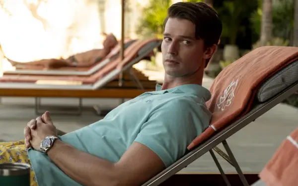 A scene from the TV show The White Lotus featuring Patrick Schwarzenegger reclining on a lounge chair by a pool, capturing a relaxed yet contemplative moment.