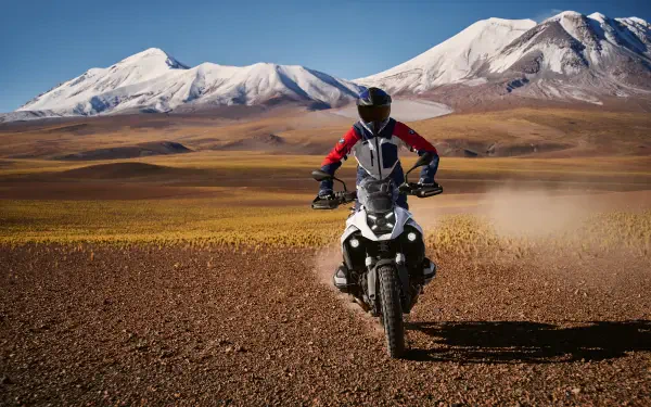 A BMW R1300GS motorcycle navigates a rugged landscape, with snow-capped mountains in the background, showcasing its prowess in motocross adventures. 4K Ultra HD wallpaper.