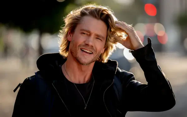 Chad Michael Murray smiles and runs his hand through his hair in this vibrant 4K Ultra HD wallpaper from the movie Freakier Friday. A lively urban background enhances the scene.