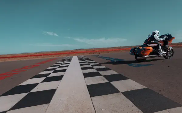 A Harley-Davidson CVO Road Glide RR takes a sharp curve on a checkered racetrack, set against a vibrant blue sky, showcasing its sleek design in this dynamic 4K Ultra HD wallpaper.