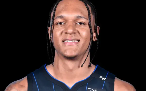 A close-up of Paolo Banchero, NBA player for the Orlando Magic, smiling confidently in his team jersey, set against a solid black background.