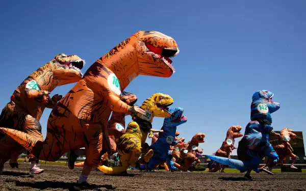 HD PC desktop wallpaper featuring a vibrant lineup of inflatable Tyrannosaurus Rex costumes against a clear blue sky.