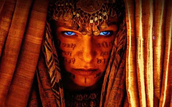 Dune: Part Two 4K Ultra HD PC desktop wallpaper — close-up of a veiled figure with glowing blue eyes, facial script tattoos and ornate headpiece framed by warm golden-orange drapery.