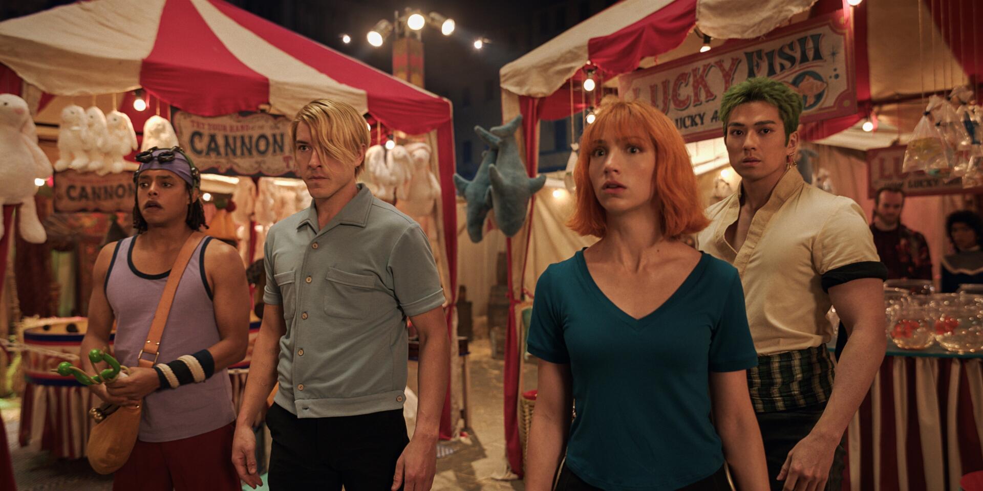 One Piece (Live Action) TV show: four characters stand tense in a carnival aisle beneath string lights, colorful tents and signs — 2K Quad HD PC desktop wallpaper/background.