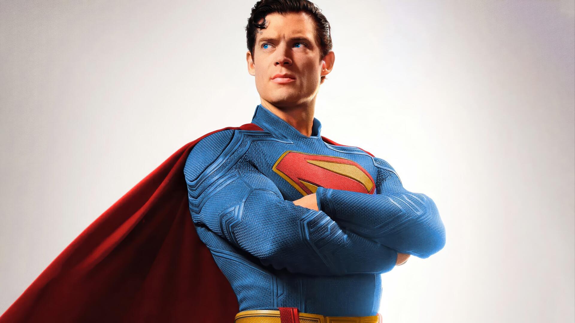 Superman (2025) in a textured blue suit and red cape, arms crossed in a heroic pose on a white backdrop — 4K Ultra HD PC desktop wallpaper/background