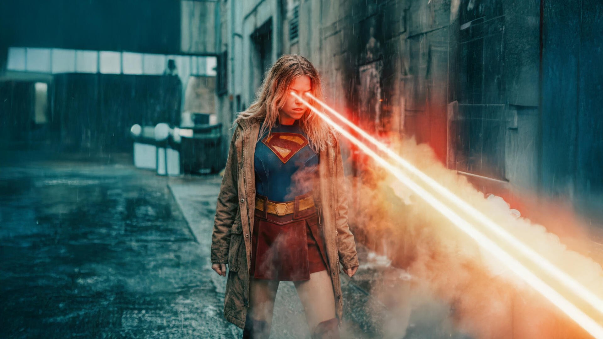 Supergirl (2026) 5K Ultra HD PC desktop wallpaper/background: Supergirl in a coat over her suit, unleashing intense red heat-vision down a smoky urban alley.