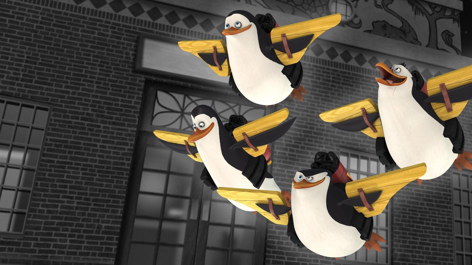 The Penguins of Madagascar in mid-flight over a brick city facade — 4K Ultra HD PC desktop wallpaper and background.