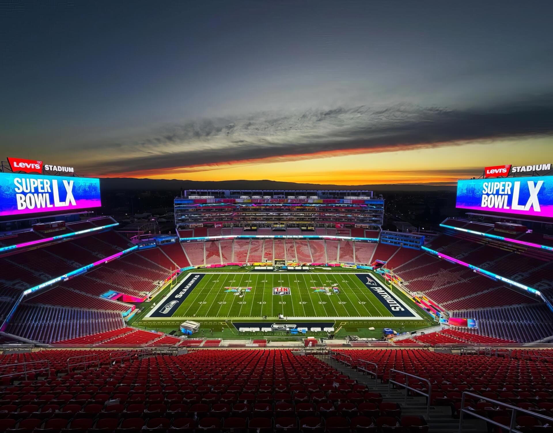 2K Quad HD PC desktop wallpaper: panoramic NFL Super Bowl stadium at sunset, illuminated football field and bright Super Bowl signage.