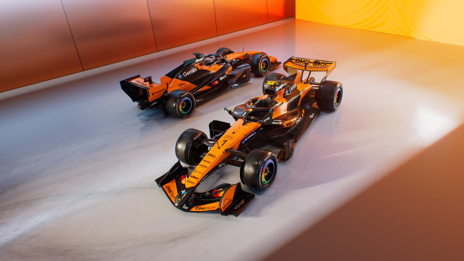 HD PC desktop wallpaper of two orange McLaren F1 race cars on a glossy studio floor bathed in warm light.