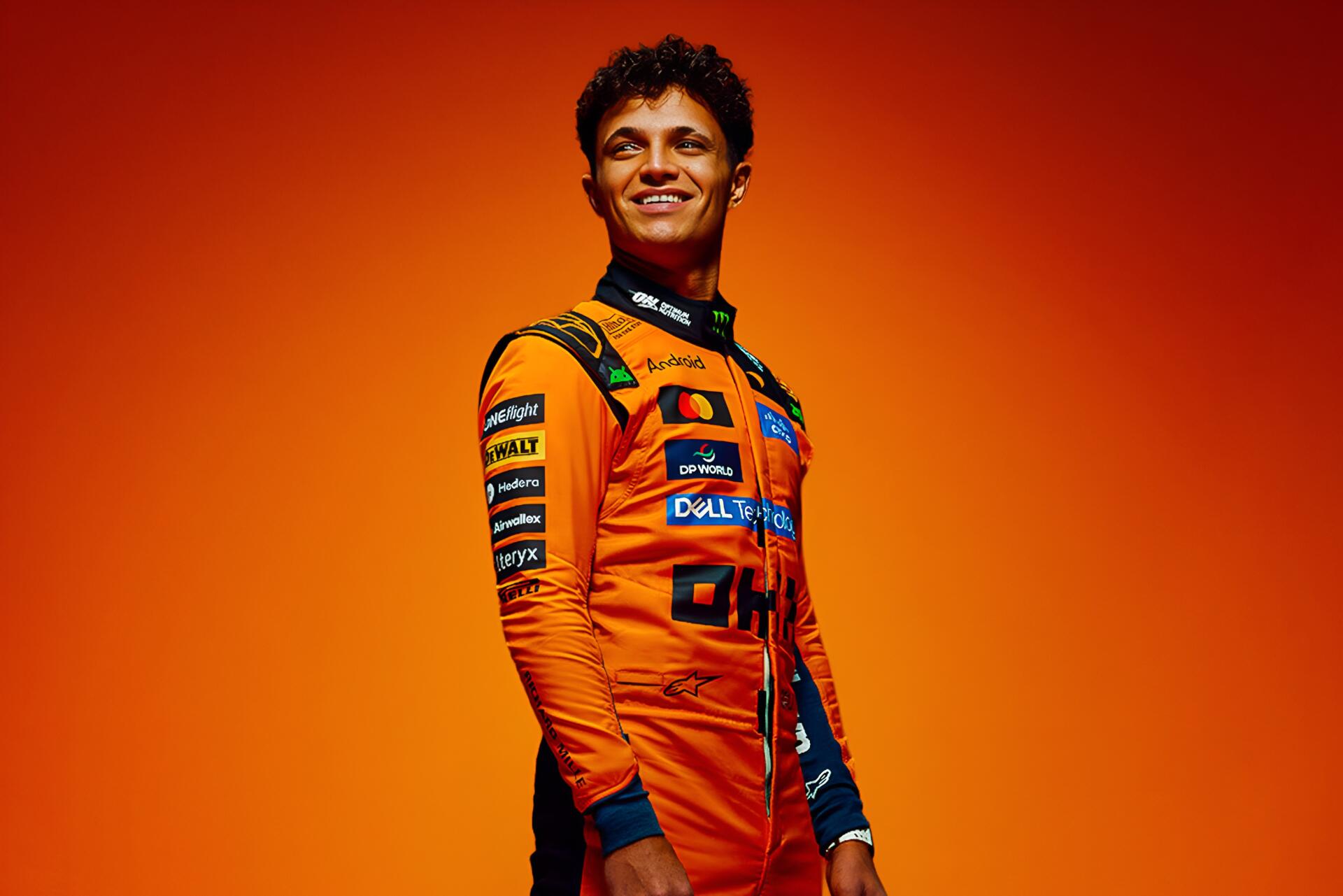 Smiling person in orange McLaren F1 racing suit against a vivid orange backdrop — 2K Quad HD desktop wallpaper.