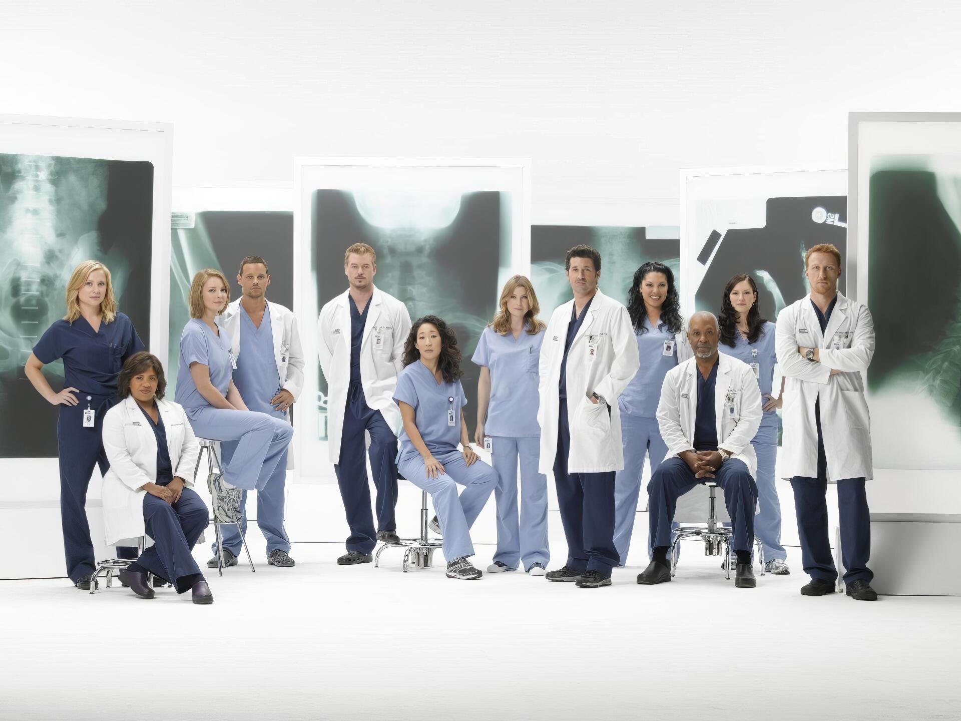 HD PC desktop wallpaper for the TV show Grey's Anatomy showing a group of doctors in scrubs and white coats posed in front of large chest X-ray panels.