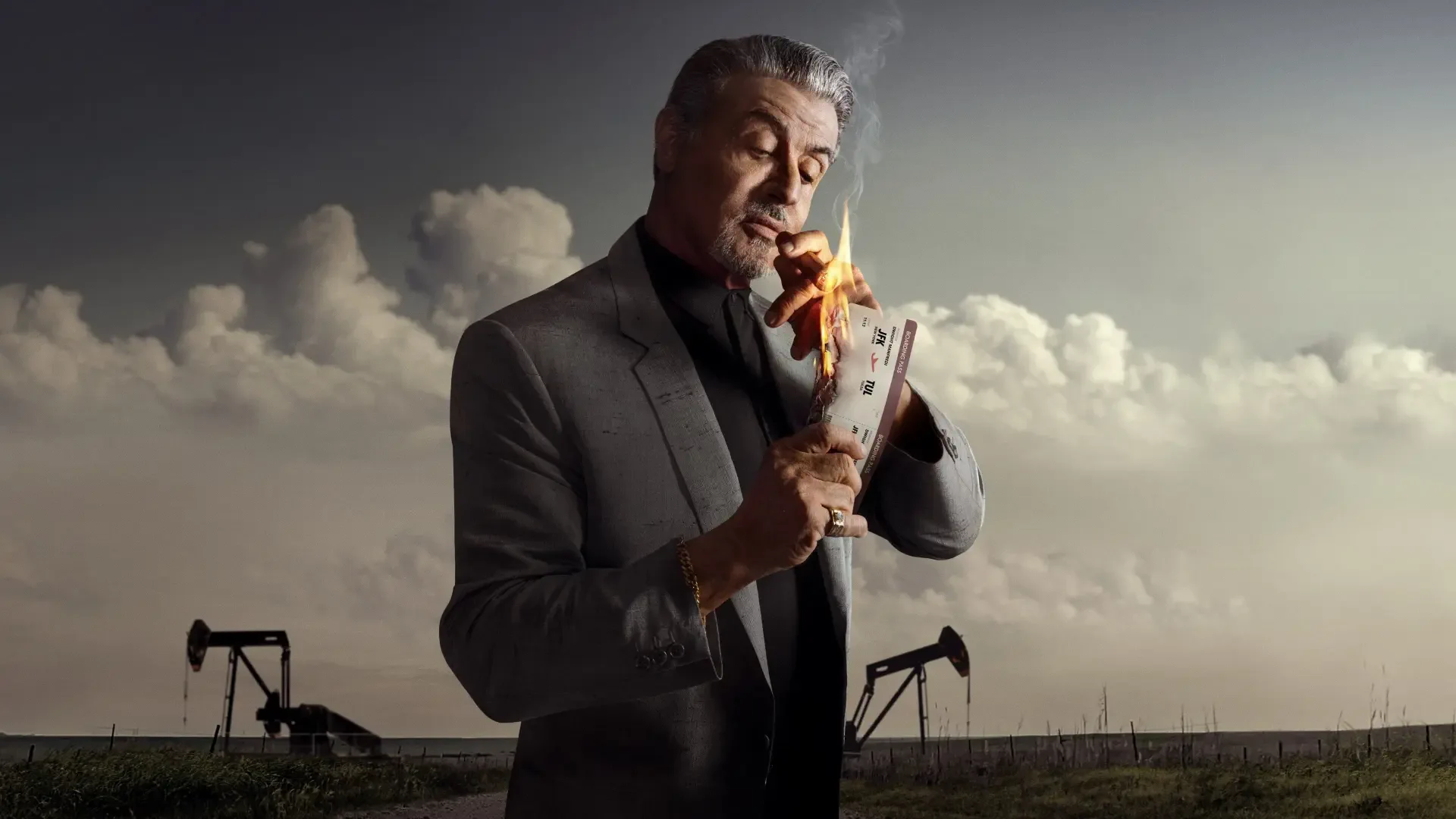 Tulsa King 4K Ultra HD PC Desktop Wallpaper and Background: gray-suited man lights a burning playing card against flatlands with oil pumpjacks beneath a dramatic cloudy sky.