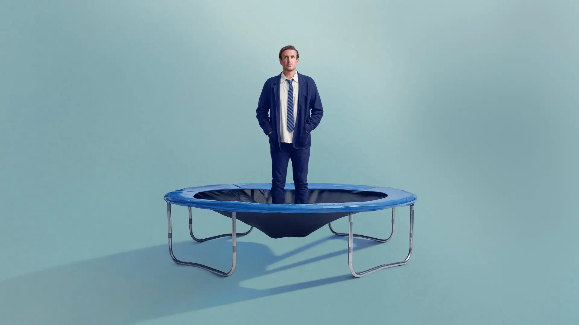 4K Ultra HD PC Desktop Wallpaper and Background: man stands on a small trampoline in a pale teal room, conveying a surreal shrinking theme.