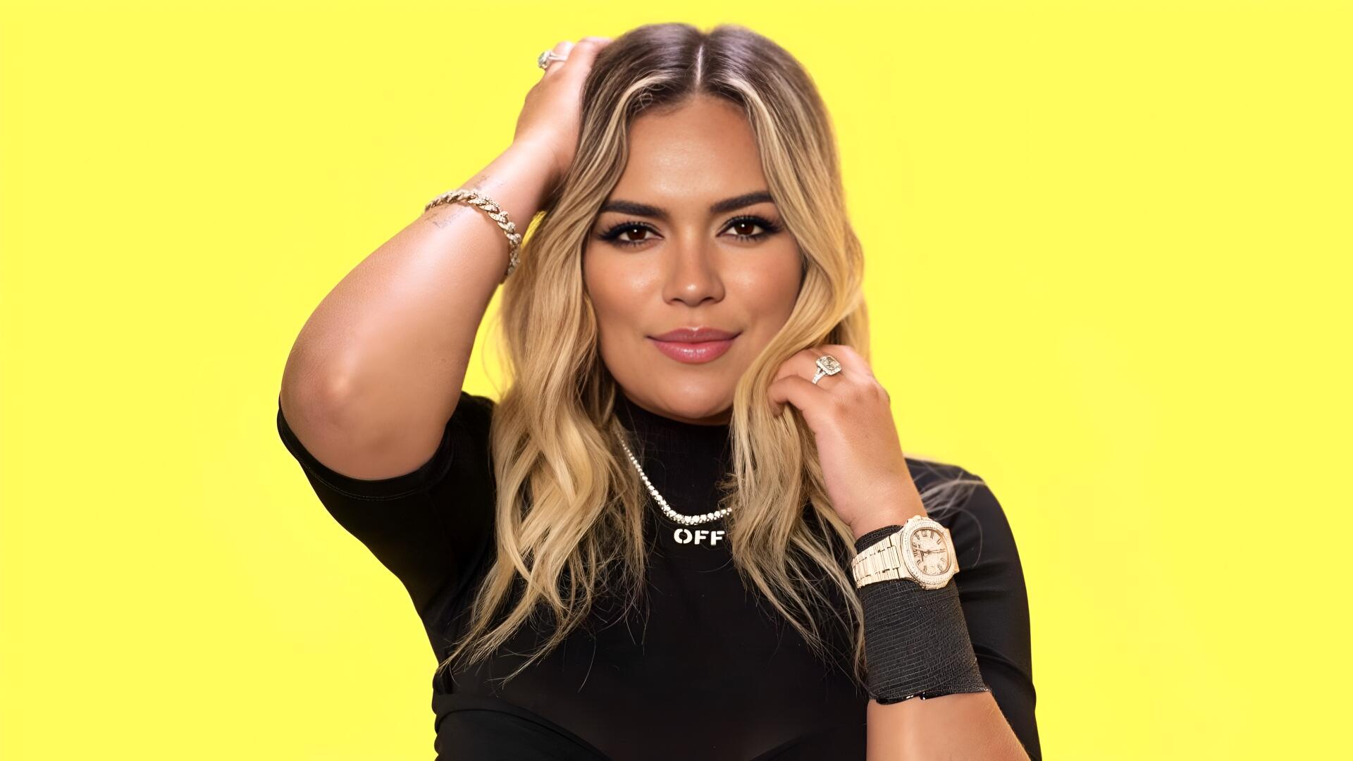 Close-up portrait of a blonde reggaeton singer celebrity against a vivid yellow backdrop, styled as a 4K Ultra HD PC desktop wallpaper.