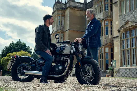 Two actors from The Thursday Murder Club exchange words beside a classic motorcycle outside a country manor — 4K Ultra HD PC desktop wallpaper.