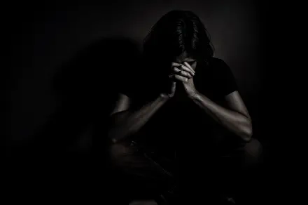 4K Ultra HD PC desktop wallpaper of a solitary figure in darkness, head bowed and hands clasped, conveying isolation and depression.