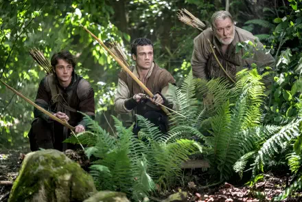 HD PC desktop wallpaper: three archers crouch amid ferns in a dense forest, scene from the TV show Robin Hood (2025).