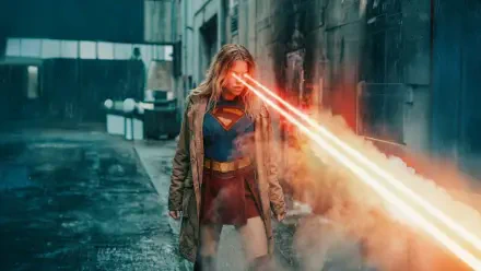 Supergirl (2026) 5K Ultra HD PC desktop wallpaper/background: Supergirl in a coat over her suit, unleashing intense red heat-vision down a smoky urban alley.
