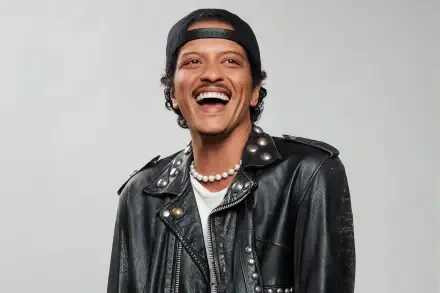 HD PC desktop wallpaper of a smiling music celebrity in a black leather jacket, backward cap and pearl necklace, posed against a light gray background.