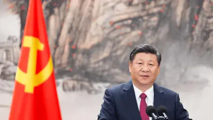 Portrait of a suited man at a podium beside a red hammer-and-sickle flag, ink-mountain backdrop — 2K Quad HD PC desktop wallpaper.