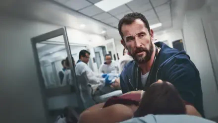 The Pitt — 4K Ultra HD PC desktop wallpaper: tense hospital corridor scene with a bearded man leaning over an injured patient on a gurney while hazmat-suited staff work in the background.