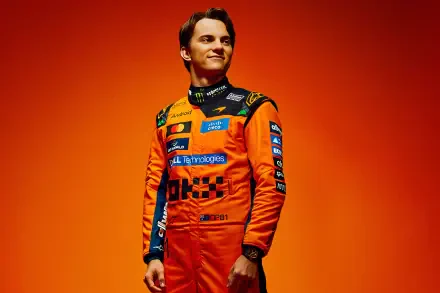 Person in orange McLaren F1 racing suit with sponsor logos on matching orange background — 2K Quad HD PC desktop wallpaper.