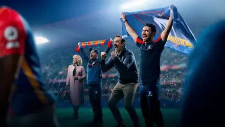 Ted Lasso and coaches cheer on a floodlit soccer pitch, scarf raised; 4K Ultra HD PC desktop wallpaper and background.