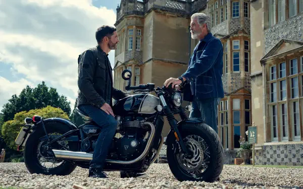 Two actors from The Thursday Murder Club exchange words beside a classic motorcycle outside a country manor — 4K Ultra HD PC desktop wallpaper.
